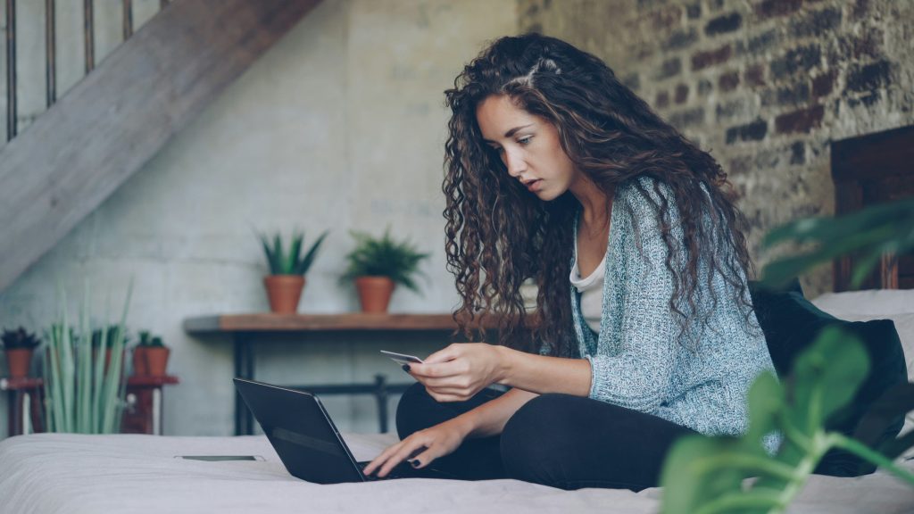 Woman using laptop and credit card on bed.